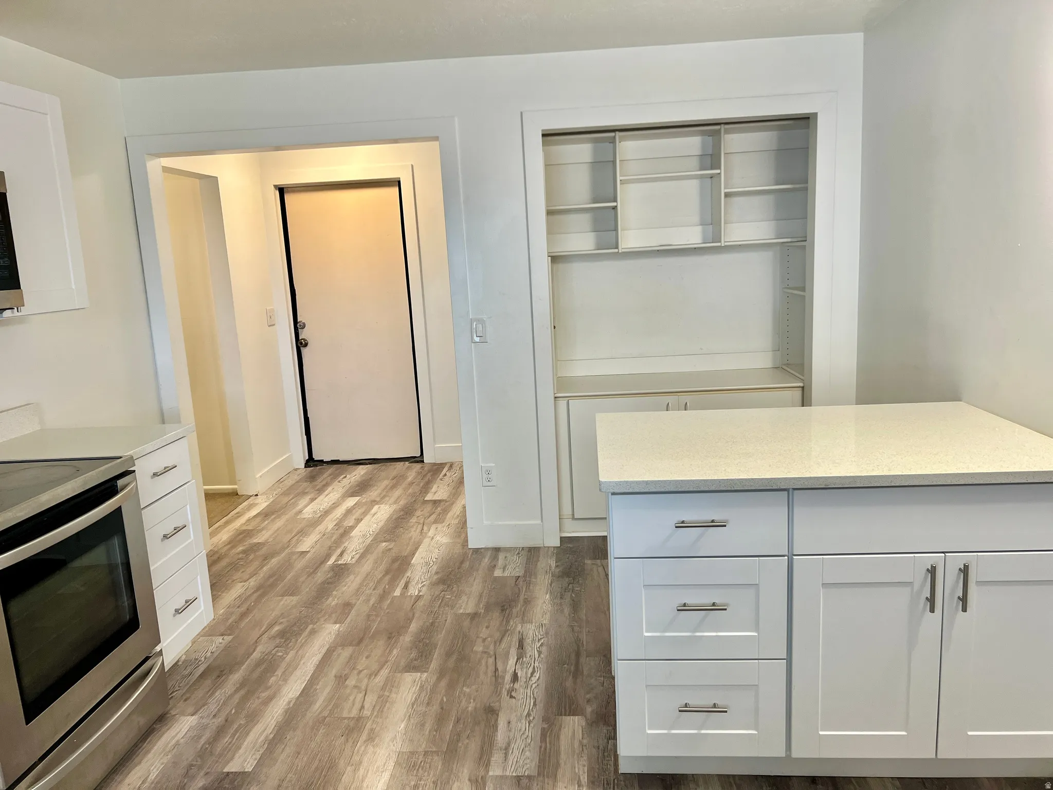 Modern kitchen featuring white cabinetry with brushed nickel hardware, light-toned countertops, stainless steel electric range, and wood-finish flooring