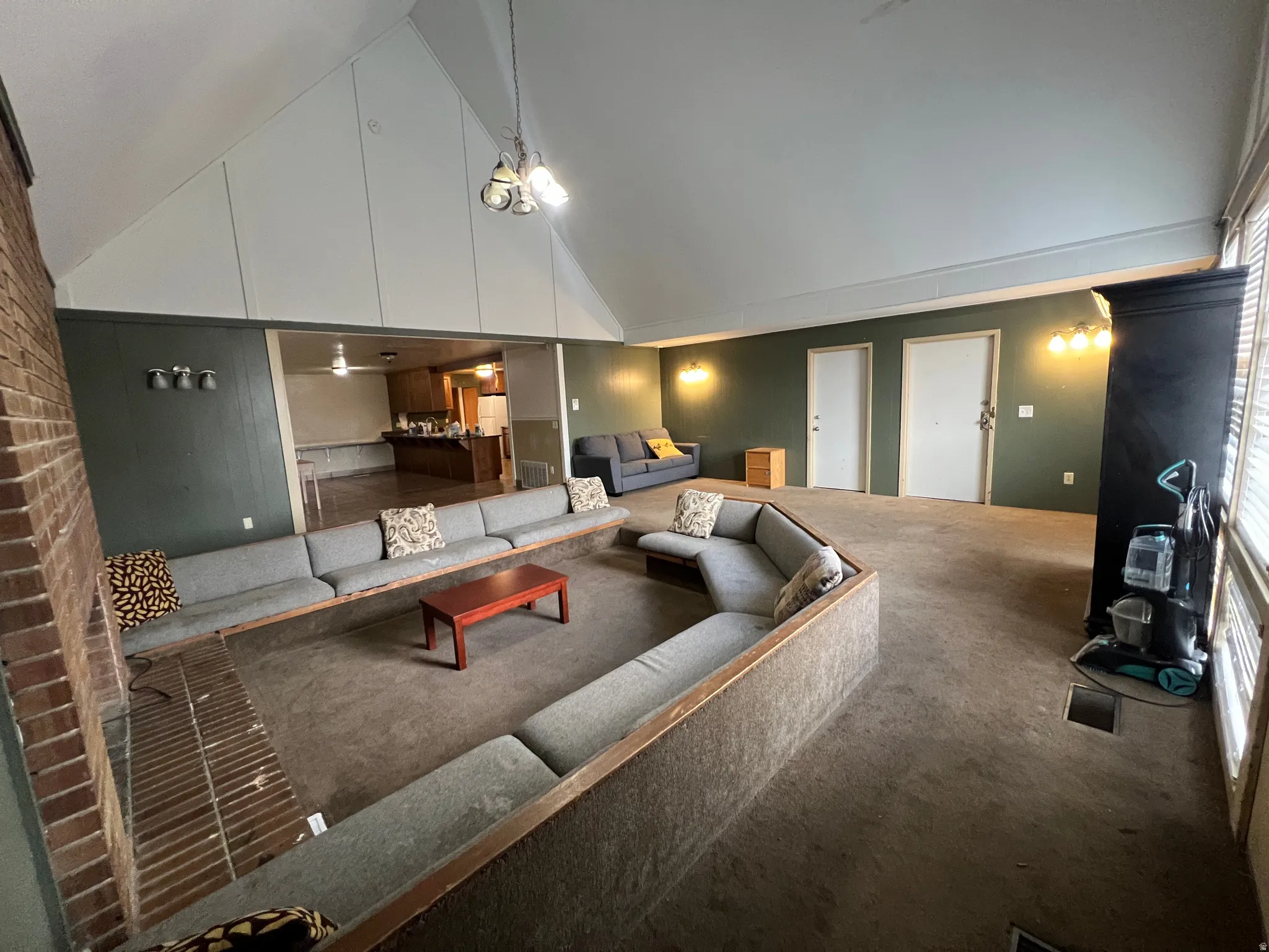 Spacious living area featuring a vaulted ceiling and exposed brickwork
