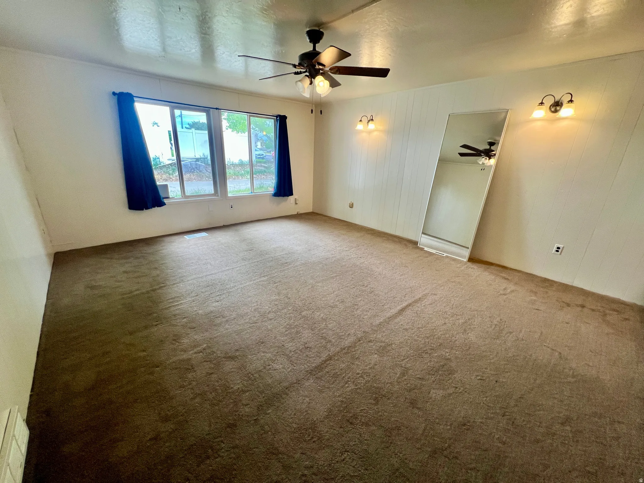 Spacious room featuring carpeting, multiple windows, wall sconces, and a ceiling fan with integrated lighting