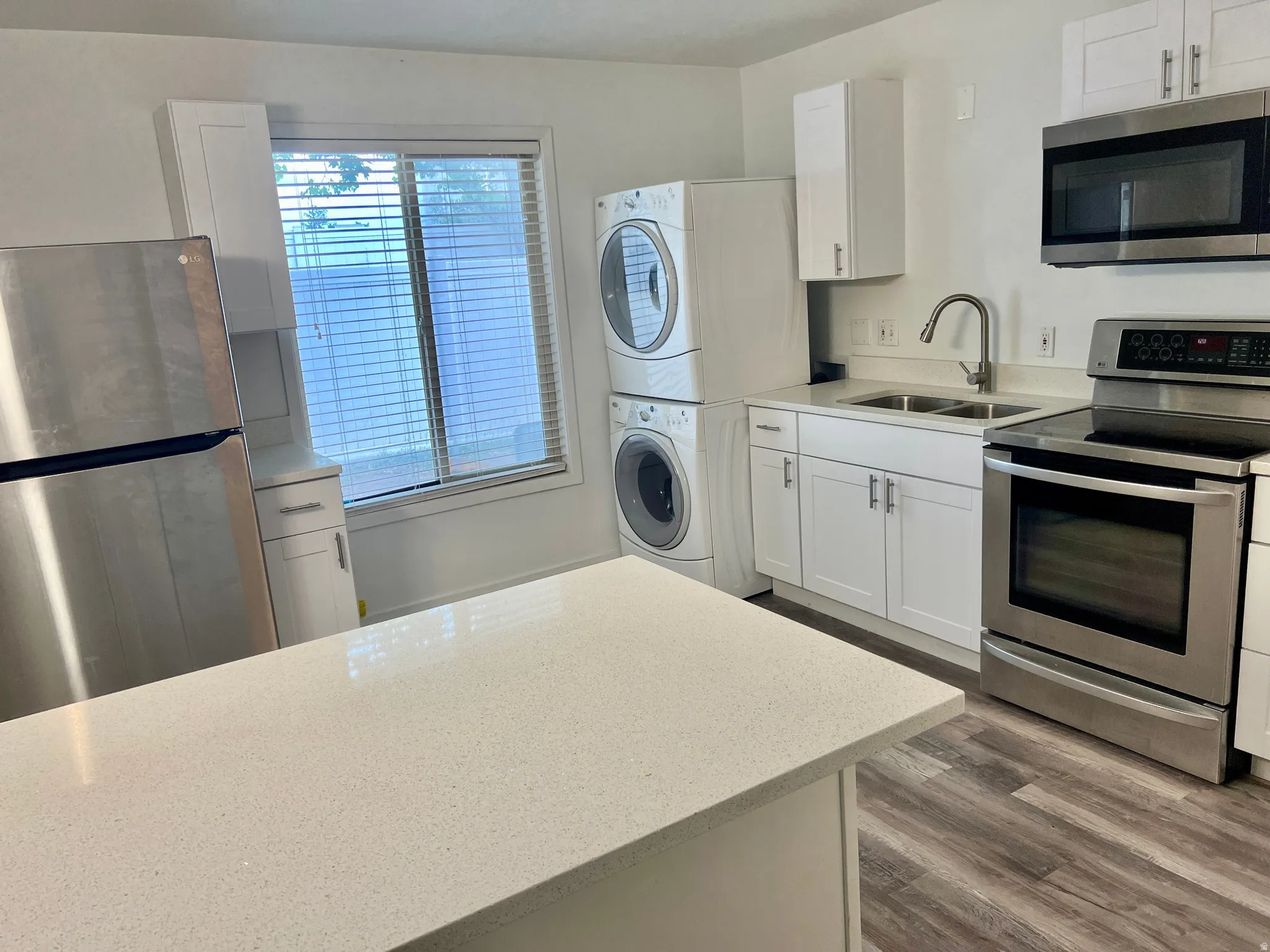 Kitchen featuring a light-toned countertop island, white shaker cabinetry, stainless steel appliances, and wood-finish flooring