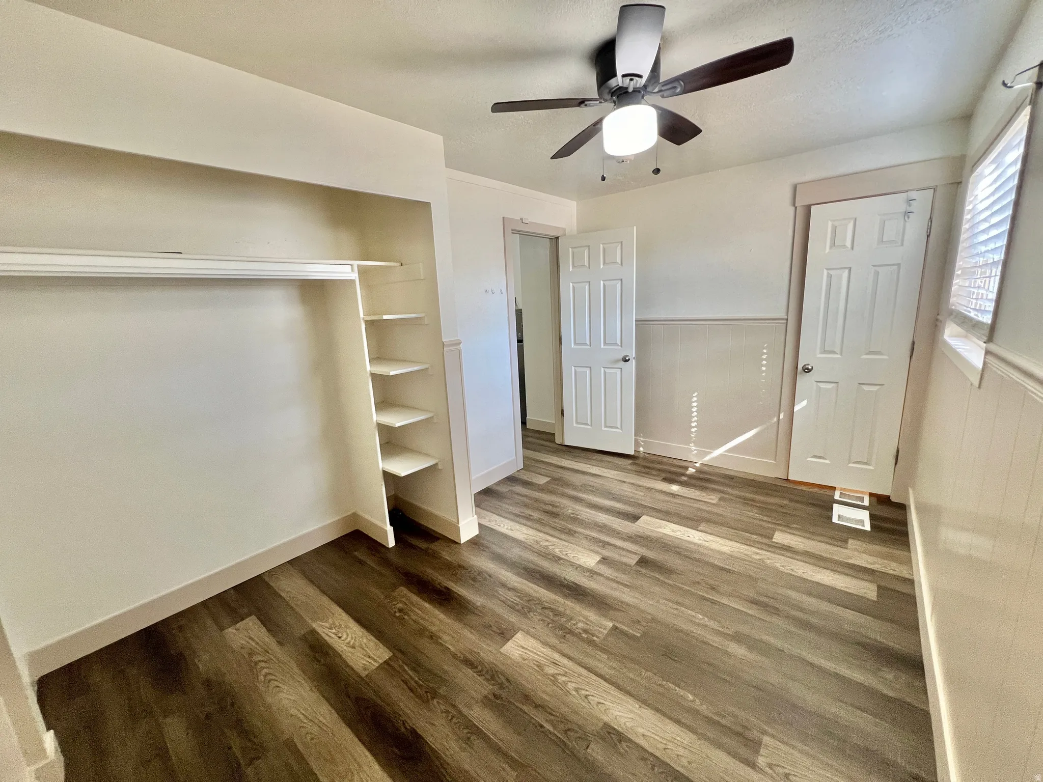 Room featuring wood-finish flooring, a built-in closet with shelving, a ceiling fan with integrated lighting, and white paneled doors