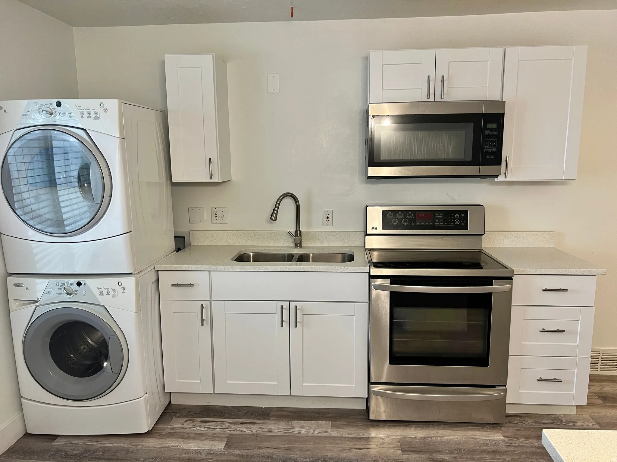 Compact kitchen area featuring white shaker cabinetry, light-toned countertops, and wood-finish flooring