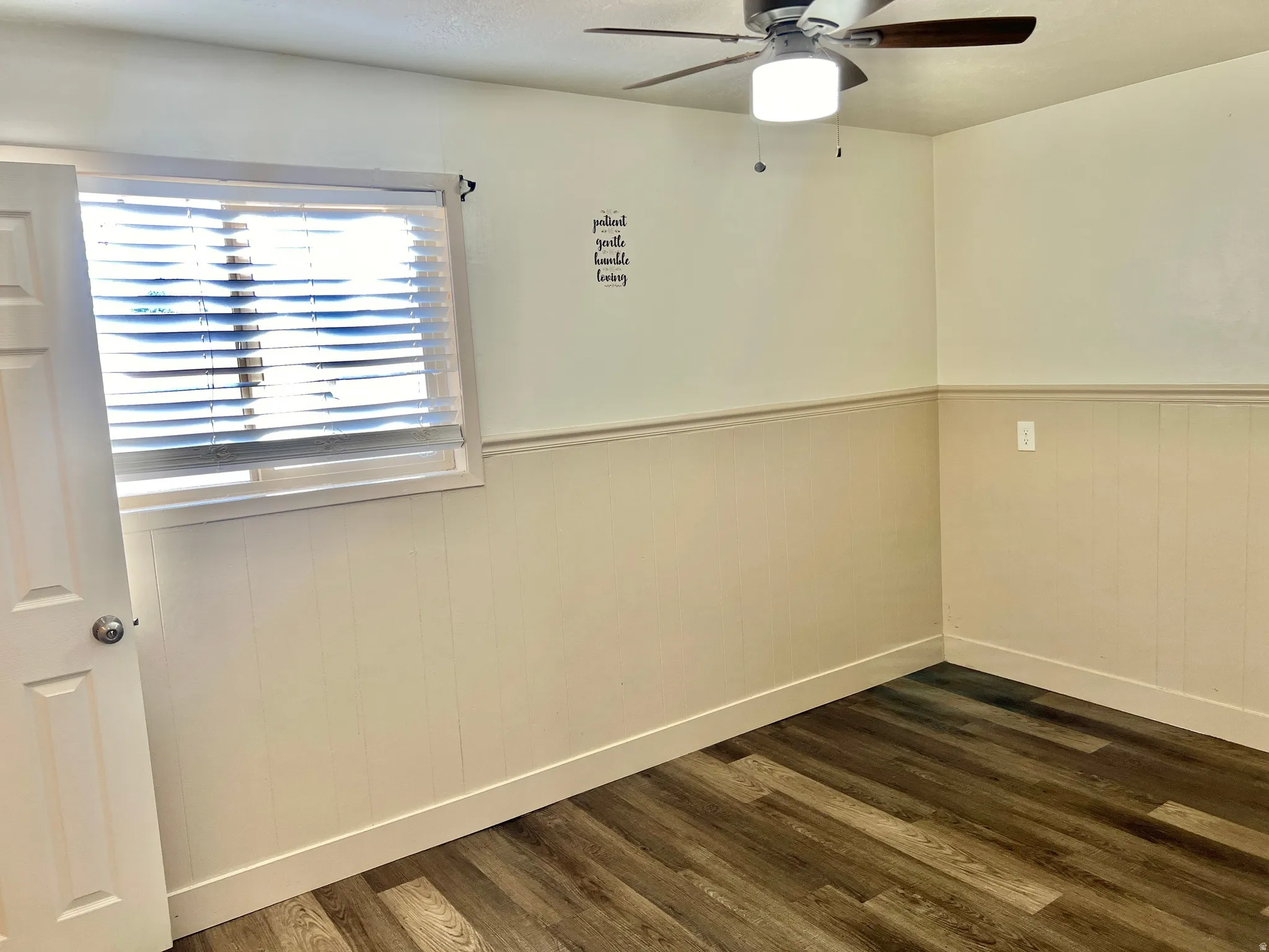 Room featuring wood-finish flooring, white paneled wainscoting, and a ceiling fan with integrated lighting