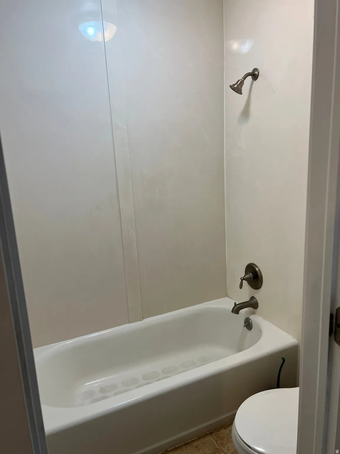 White bathtub and shower combination with a bronze-finish showerhead and faucet