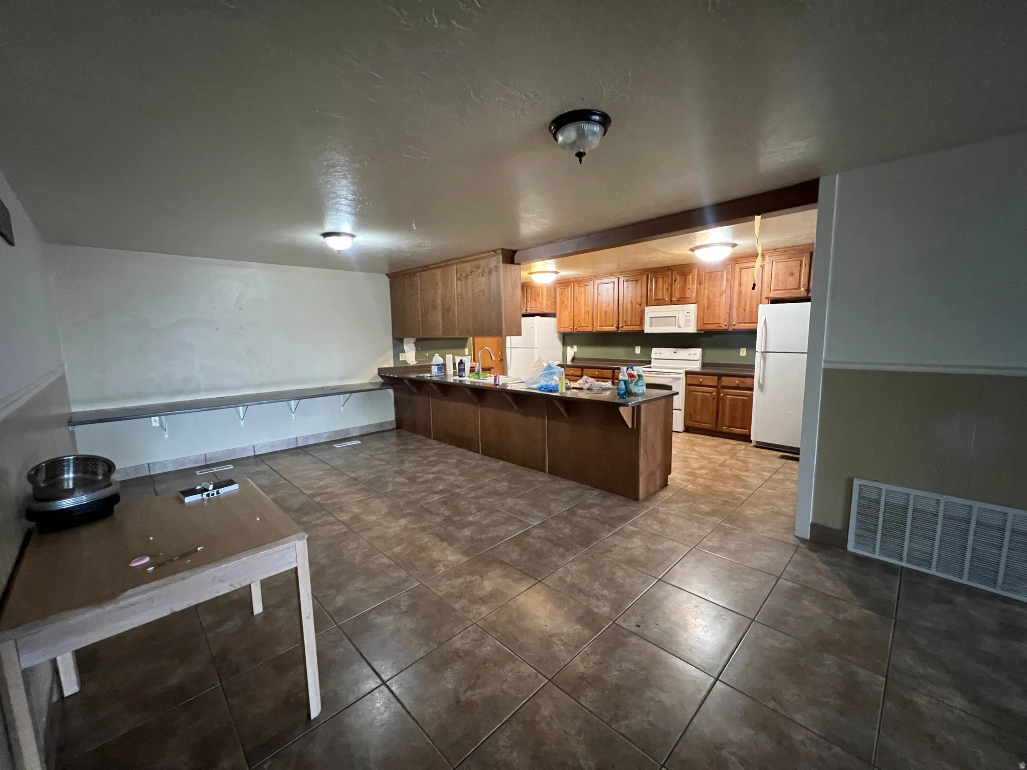 Open-concept kitchen and dining area featuring tile flooring, wooden cabinetry, built-in shelving, and white appliances