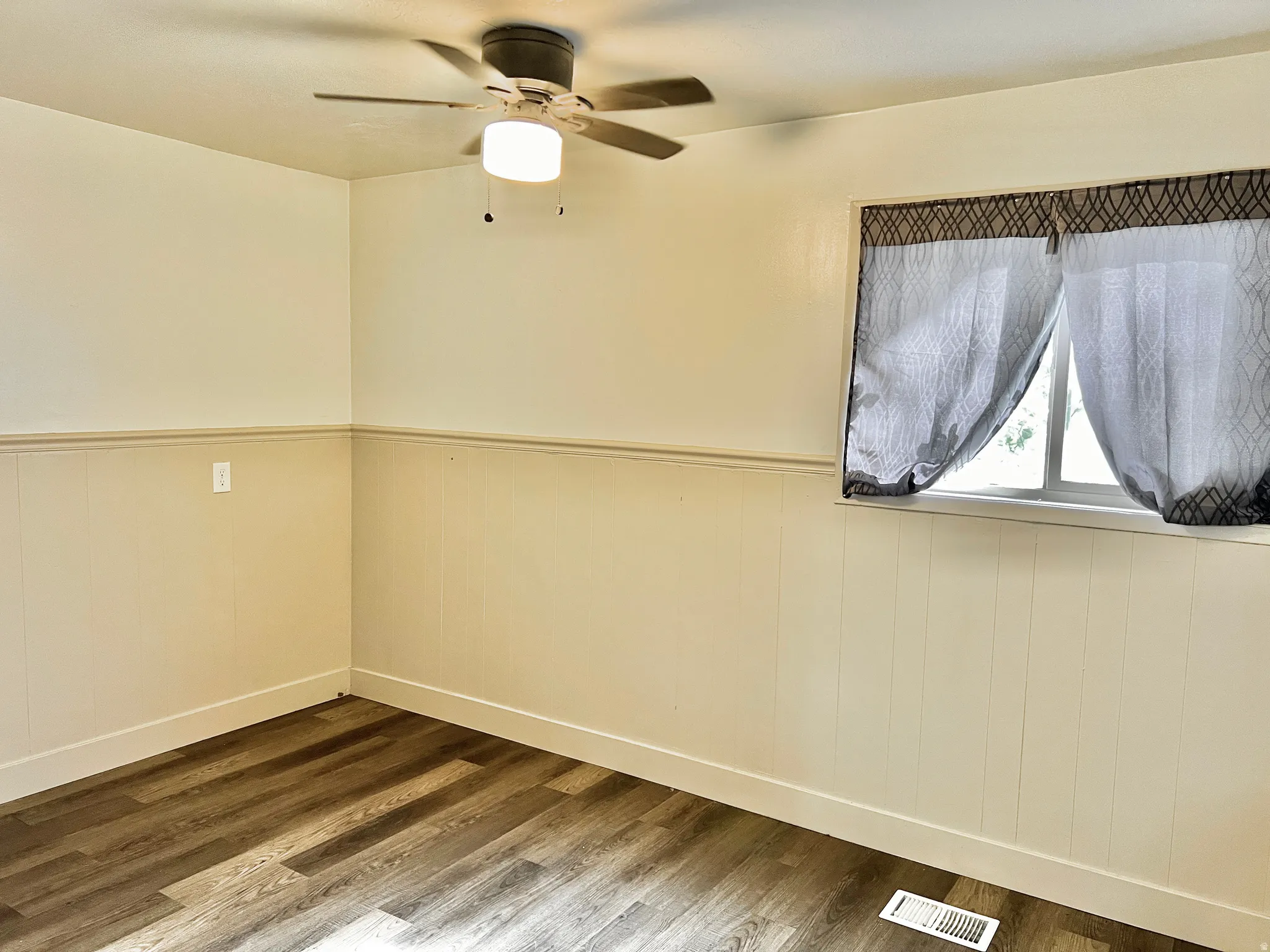 Room featuring wood-finish flooring, white baseboards, and neutral-toned wainscoting