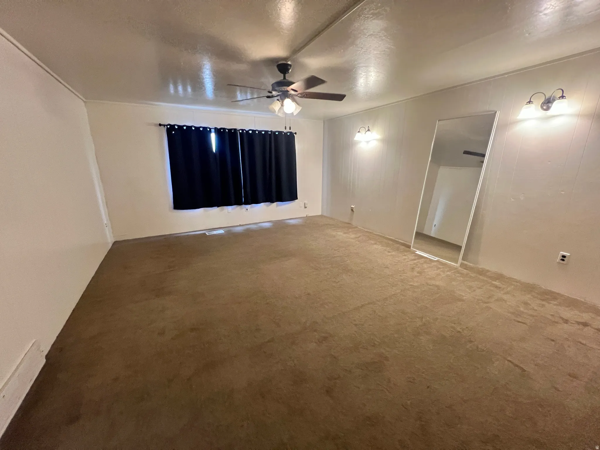Spacious room featuring neutral carpeting, a ceiling fan with integrated lighting, and two wall-mounted light fixtures