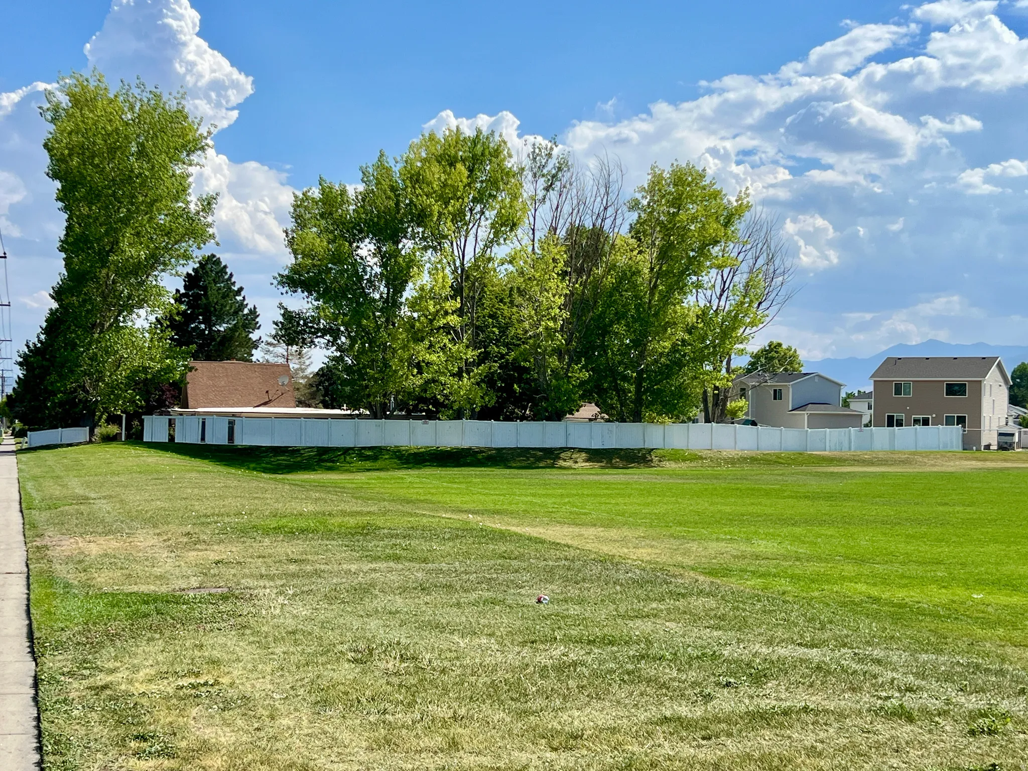Expansive green space featuring a concrete sidewalk and a white privacy fence