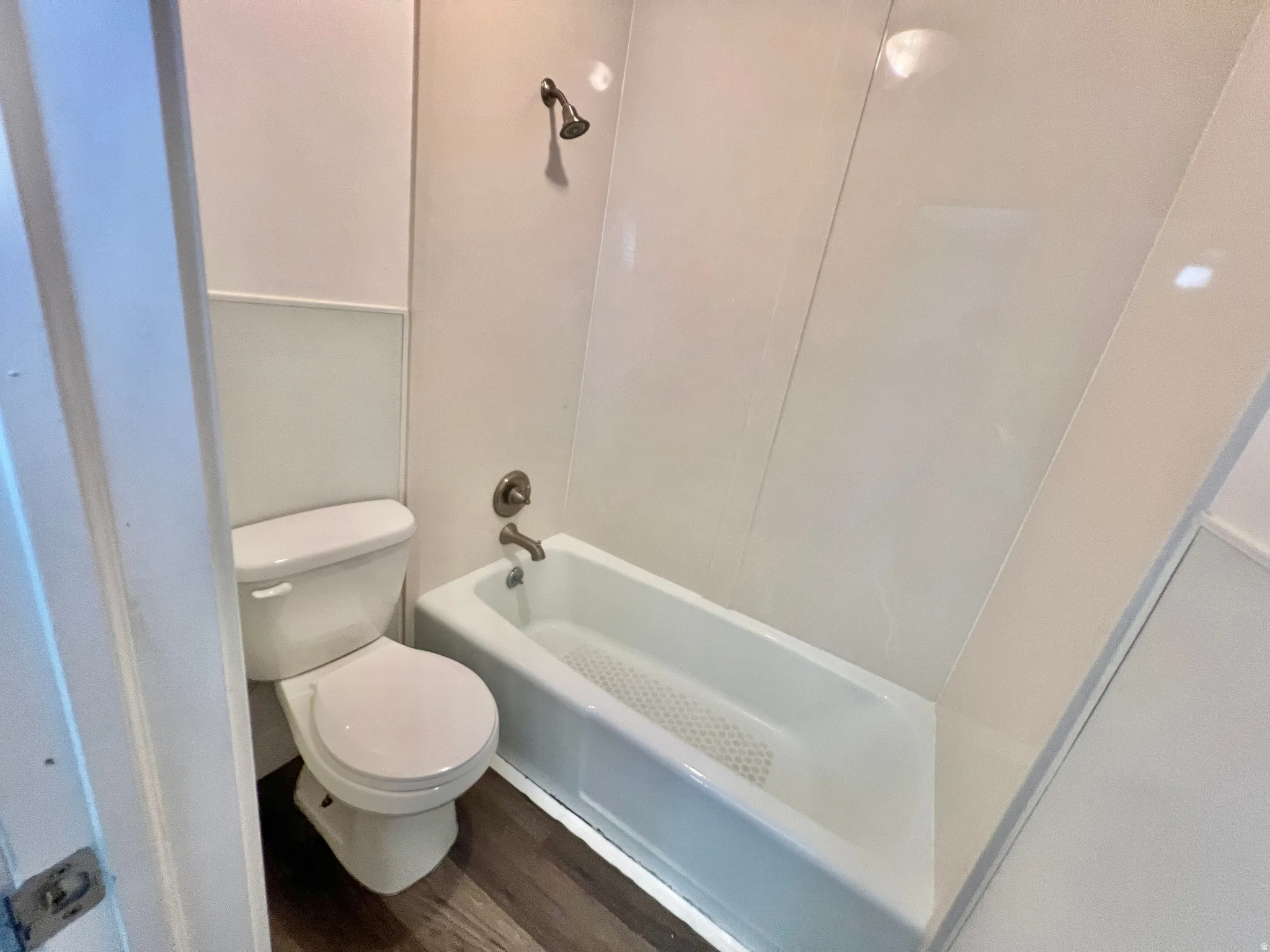 Full bathroom featuring a white porcelain toilet, white tub-shower combination, brushed nickel fixtures, and wood-finish flooring