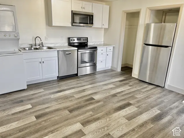 Kitchen featuring wood-finish flooring, white cabinetry, stainless steel appliances, and a stackable washer and dryer unit