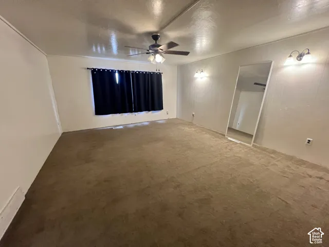 Spacious room featuring neutral carpeting, a ceiling fan with integrated lighting, and two wall-mounted light fixtures