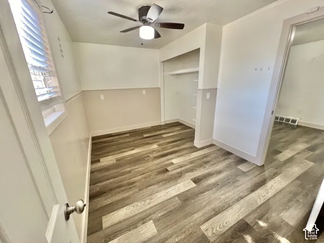 Interior room featuring wood-finish flooring, a built-in closet with shelving, and a ceiling fan with integrated lighting