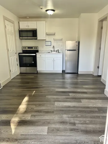 Kitchenette featuring white cabinetry, stainless steel appliances, wood-finish flooring, and a ceiling-mounted light fixture