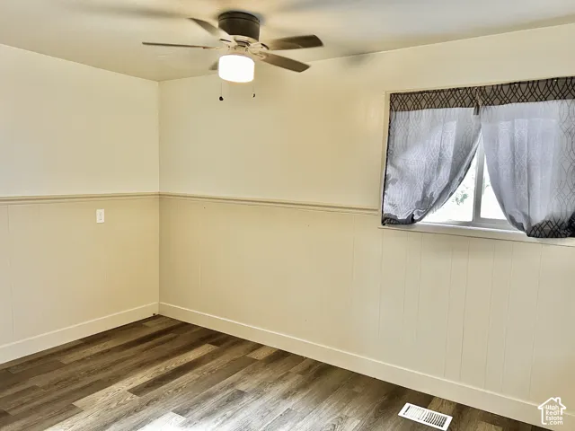 Room featuring wood-finish flooring, white baseboards, and neutral-toned wainscoting