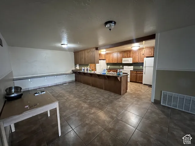 Open-concept kitchen and dining area featuring tile flooring, wooden cabinetry, built-in shelving, and white appliances