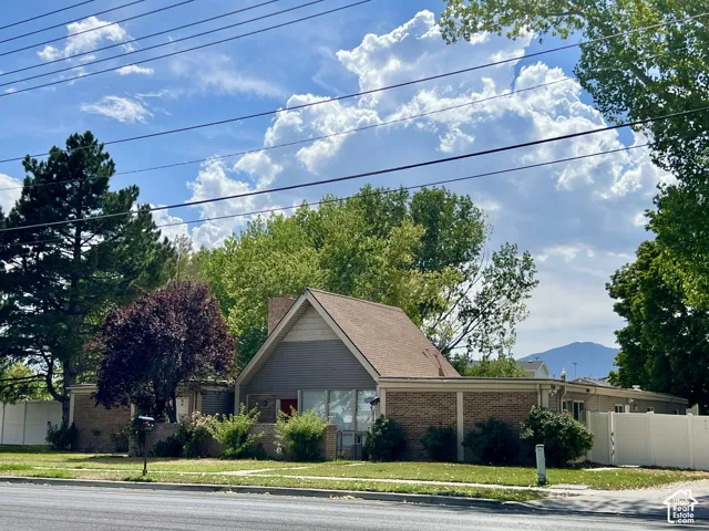 Property featuring brick and siding exterior, a pitched roof, mature landscaping, and a white privacy fence