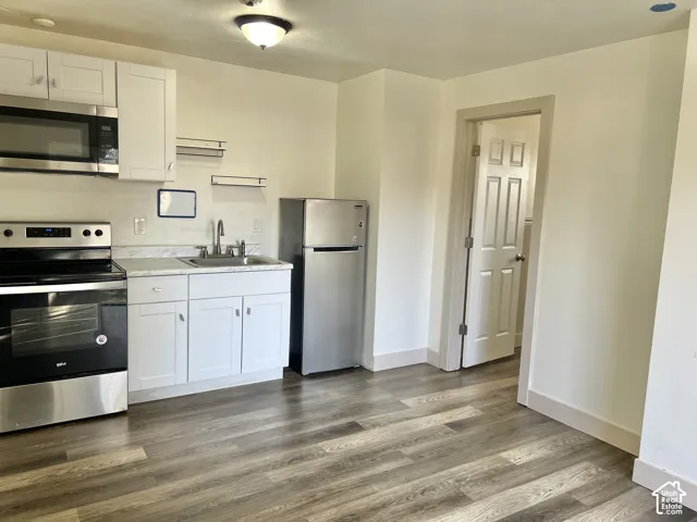Kitchenette featuring a stainless steel appliance suite, white shaker cabinetry, light-toned countertops, wood-finish flooring, and a flush-mount ceiling light fixture