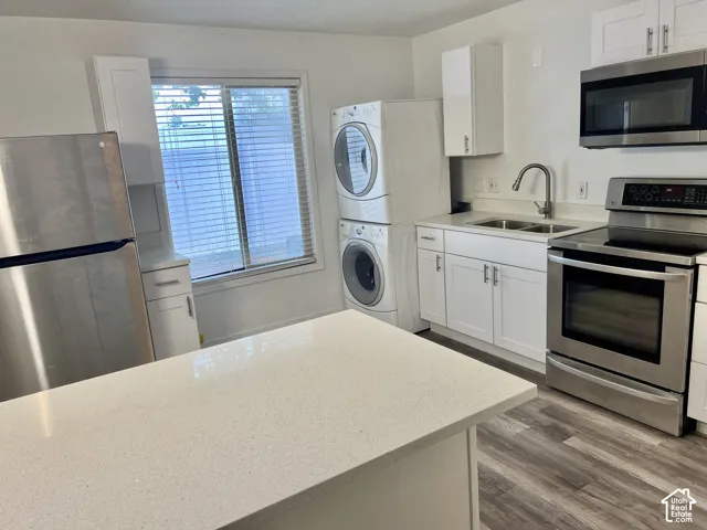 Kitchen featuring a light-toned countertop island, white shaker cabinetry, stainless steel appliances, and wood-finish flooring