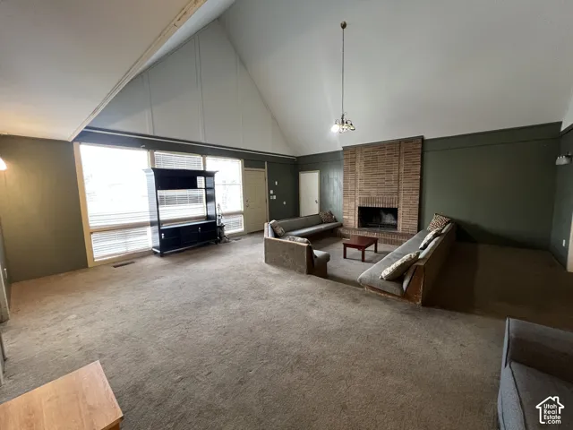 Spacious living area featuring a vaulted ceiling with exposed beams, an expansive brick fireplace, and large windows with horizontal blinds