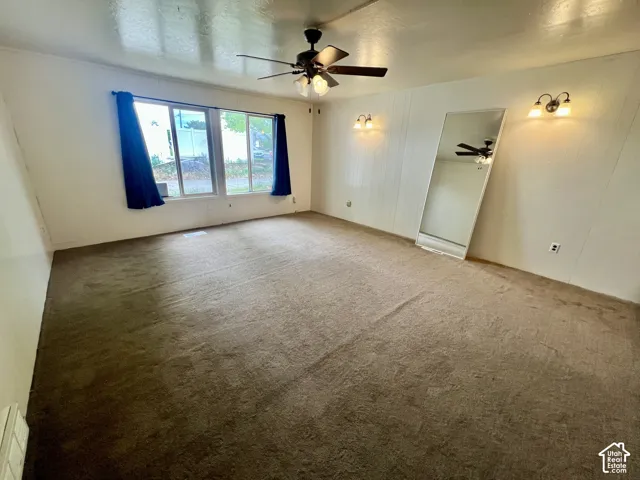 Spacious room featuring carpeting, multiple windows, wall sconces, and a ceiling fan with integrated lighting