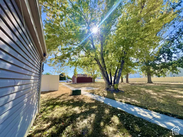 Expansive side yard featuring mature trees, a concrete pathway, and a vinyl-sided building with gutters