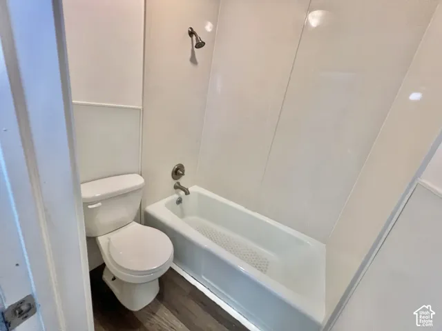 Full bathroom featuring a white porcelain toilet, white tub-shower combination, brushed nickel fixtures, and wood-finish flooring