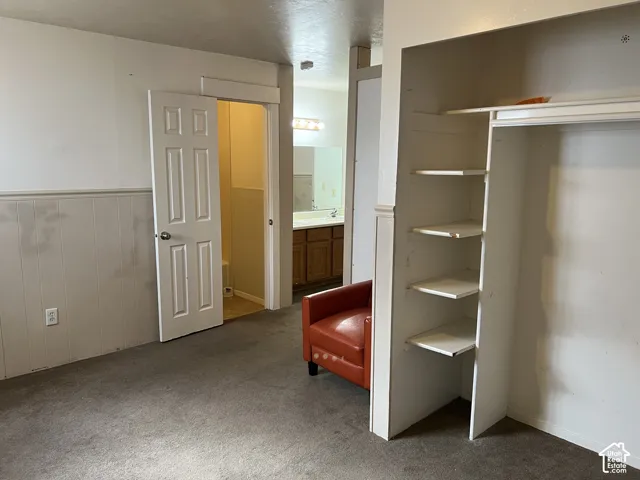 Carpeted interior space featuring white paneled wainscoting, an integrated open closet with shelving, and a six-panel interior door