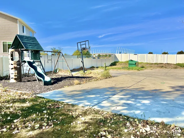 Expansive concrete patio area with a dedicated play structure, swing set, and basketball hoop