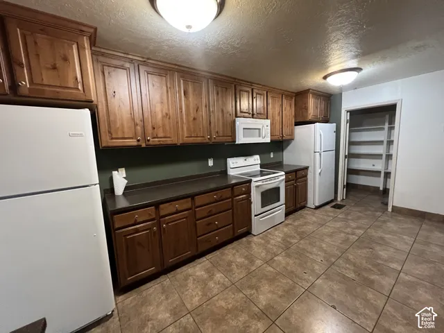 Kitchen featuring extensive wood cabinetry, dark countertops, white appliance suite, and tiled flooring