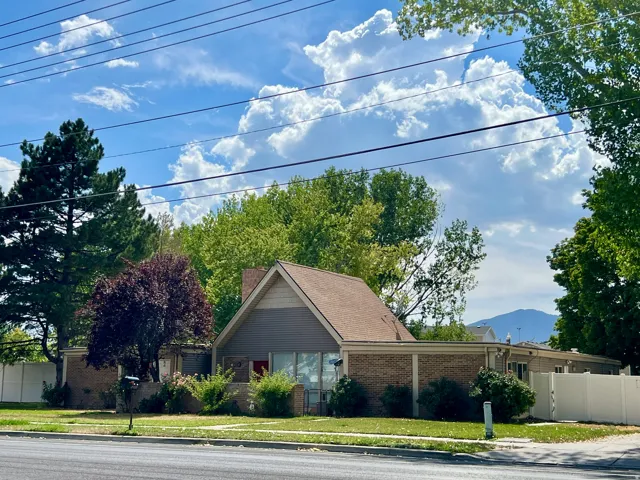 Property featuring brick and siding exterior, a pitched roof, mature landscaping, and a white privacy fence