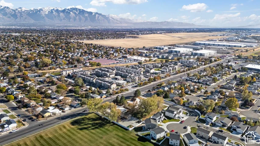 Expansive aerial perspective showcasing a residential community with varied architectural styles, a large green space, and distant mountain ranges