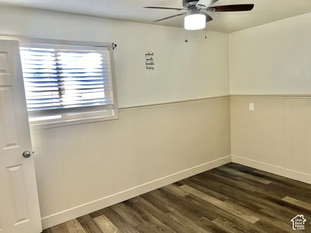 Room featuring wood-finish flooring, white paneled wainscoting, and a ceiling fan with integrated lighting