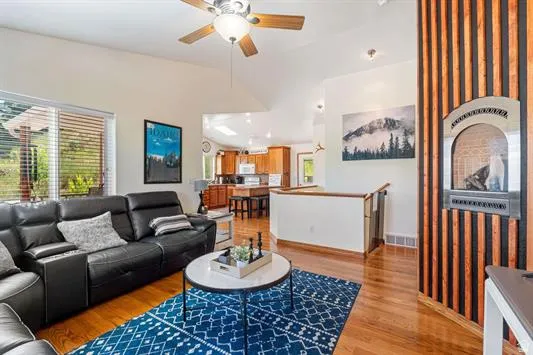 Vaulted living room with wood-finish flooring, a wall-mounted fireplace featuring wood paneling, and large windows
