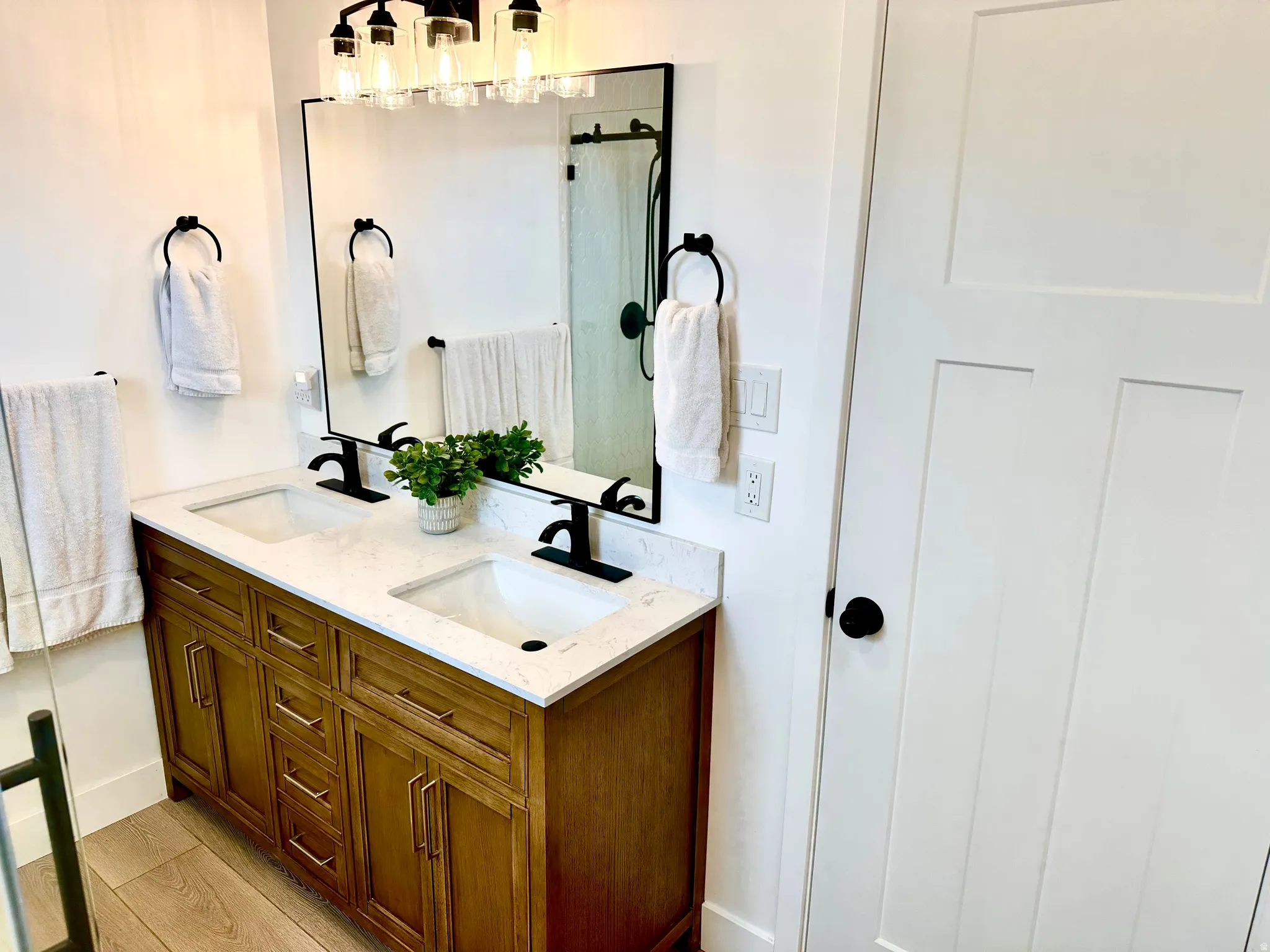 Double vanity with a light wood-finish cabinet and white countertop, featuring dual sinks and matte black fixtures