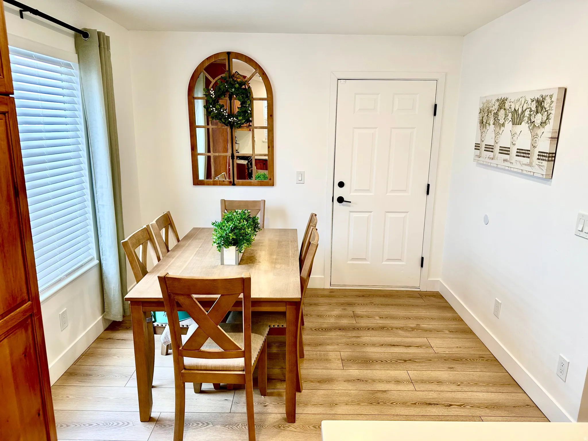 Dining area featuring wood-finish flooring, white baseboards, a white paneled door with black hardware, and a window with blinds