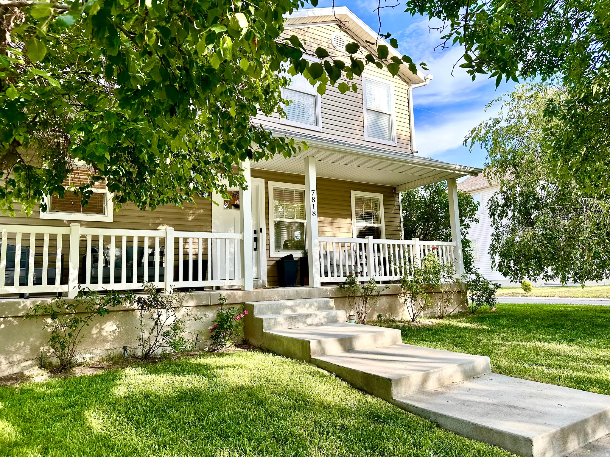 Two-story residence featuring light-toned siding, a welcoming covered front porch with white railings, and a concrete walkway