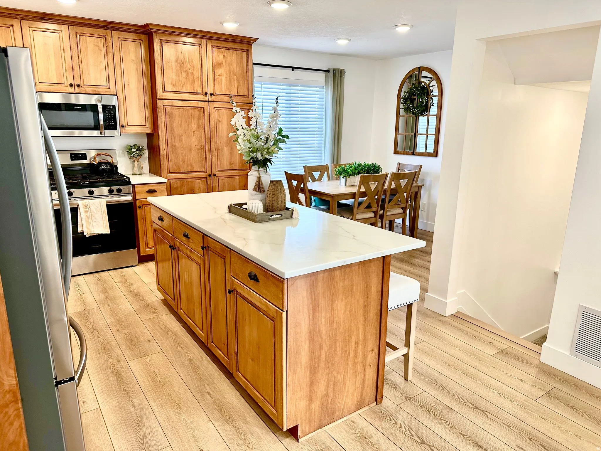 Kitchen featuring a large central island with a light-colored countertop, rich wood cabinetry, stainless steel appliances, wood-finish flooring, and recessed lighting