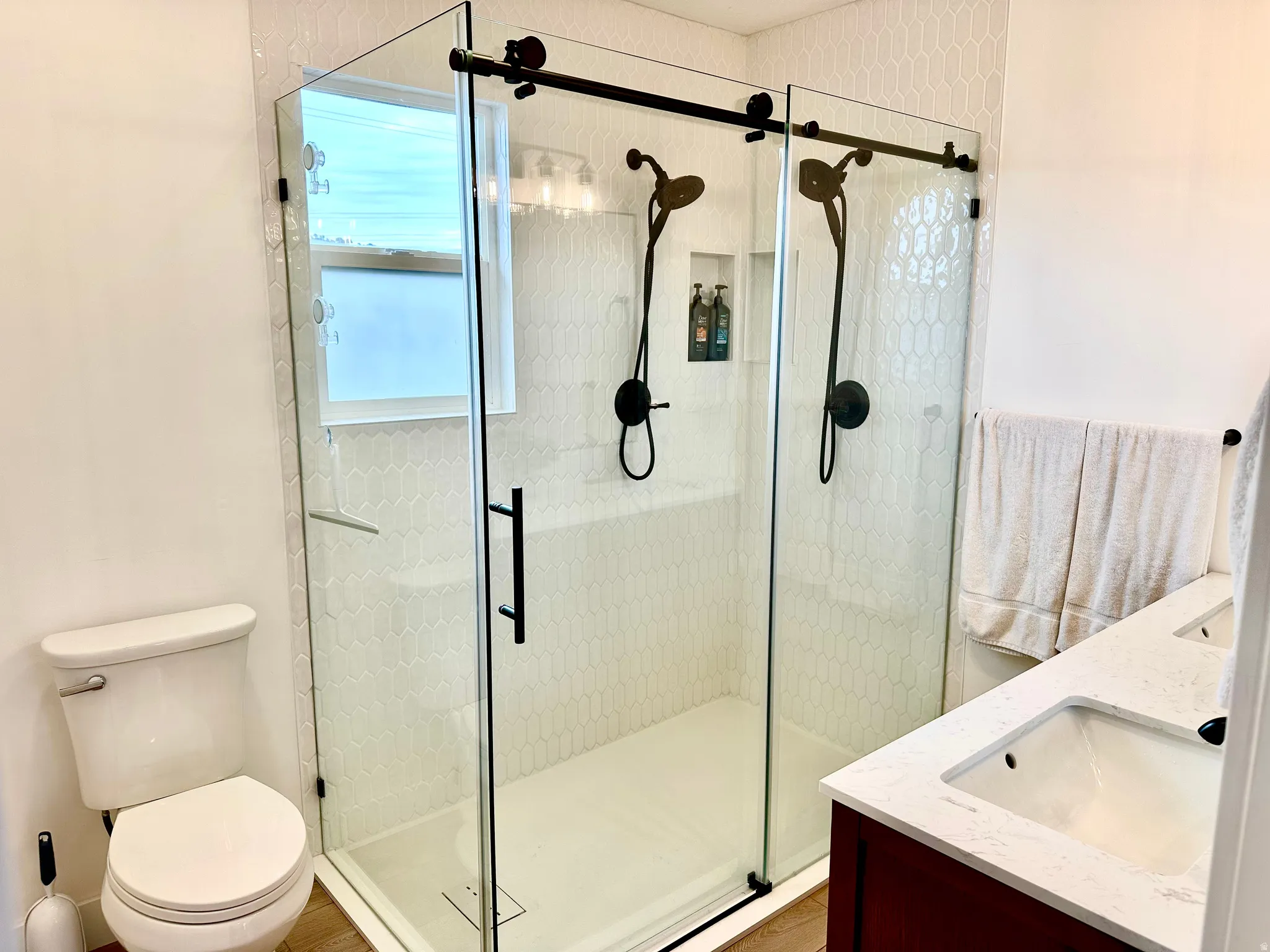 Frameless glass shower enclosure featuring dual matte black shower heads and a built-in niche