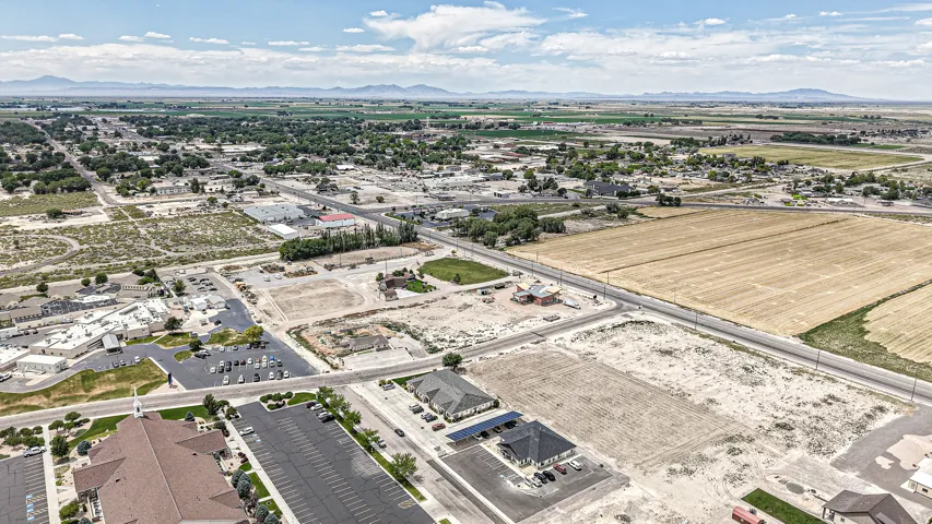 Expansive aerial landscape featuring a mix of developed and undeveloped land, established tree-lined streets, distant mountain ranges, and numerous paved parking areas