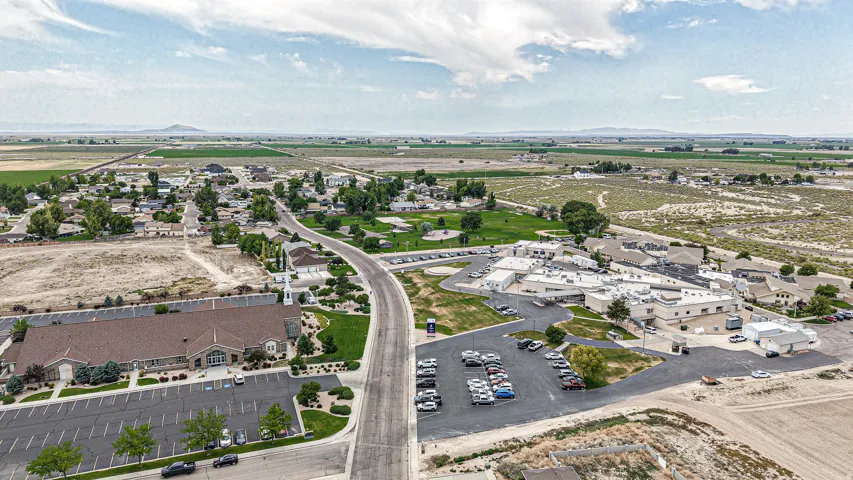 Aerial landscape featuring a developed community with residential areas, a large building with a brown roof and steeple, and a complex of commercial/institutional buildings with white roofs