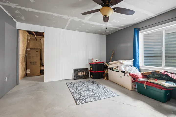 Unfinished room featuring a concrete floor, partial white beadboard wall paneling, and a ceiling fan with light fixture