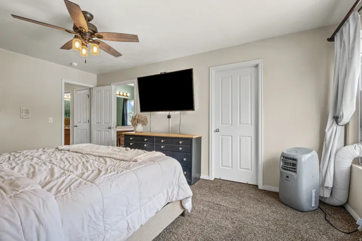 Carpeted bedroom featuring a ceiling fan with integrated lighting, a wall-mounted television bracket, and two panel doors providing access to separate areas