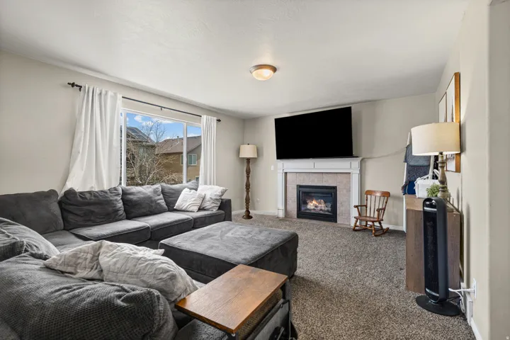 Living area featuring a gas fireplace with a tiled surround and white mantel, a large window, wall-to-wall carpeting, and neutral wall paint