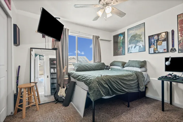 Carpeted room featuring a ceiling fan with light fixture, a window with curtains, and a built-in closet with a white door