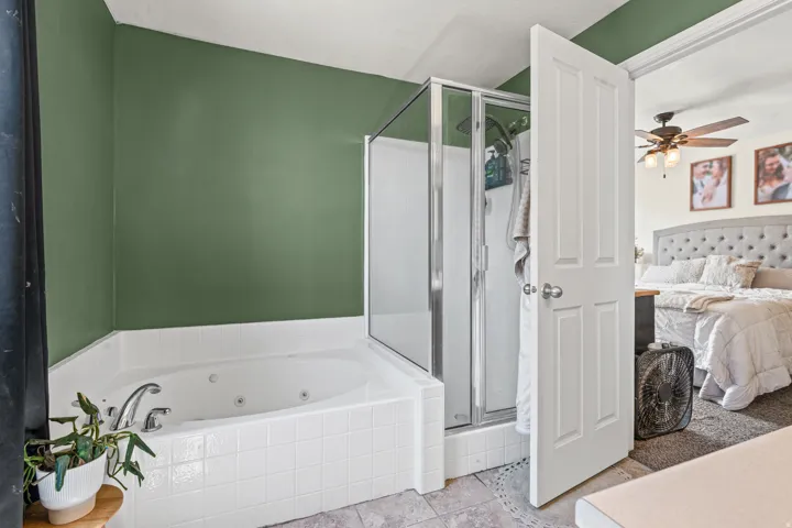 Corner jetted tub with white tile surround, adjacent to a glass-enclosed shower with chrome frame