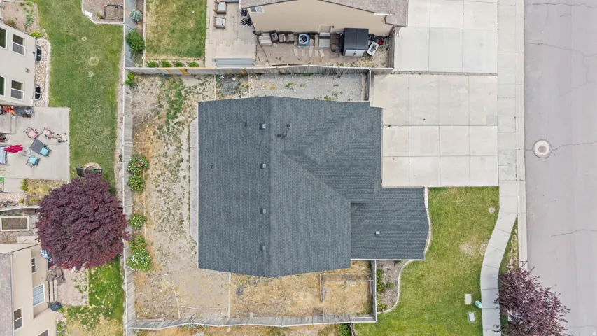 Overhead property perspective showcasing a dark shingle roof, a concrete driveway, a paved sidewalk, and a street