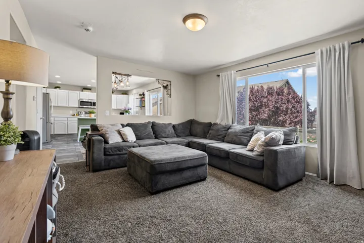 Spacious living area featuring carpet flooring, a large window, and an open pass-through to the kitchen with white cabinetry, stainless steel appliances, and tile flooring