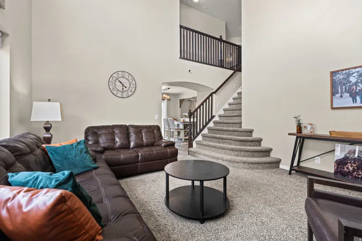 Spacious living area featuring a two-story ceiling, a carpeted staircase with dark wood railings, and an arched entry to an additional room