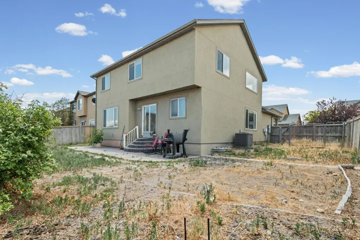 Rear exterior featuring an expansive yard, ground-level concrete patio, and upper-level sliding glass door access