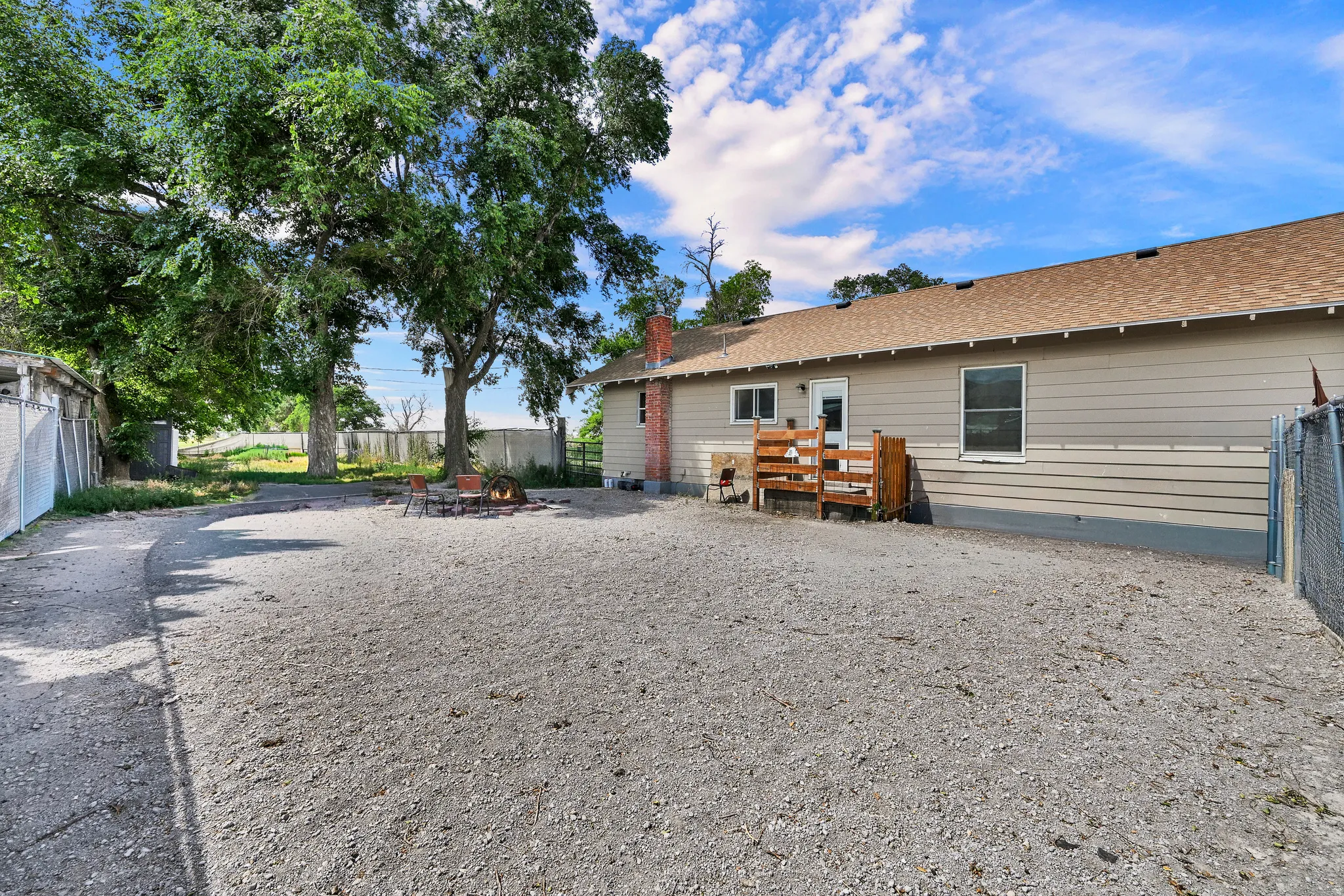 Spacious gravel yard featuring mature trees and a fire pit area